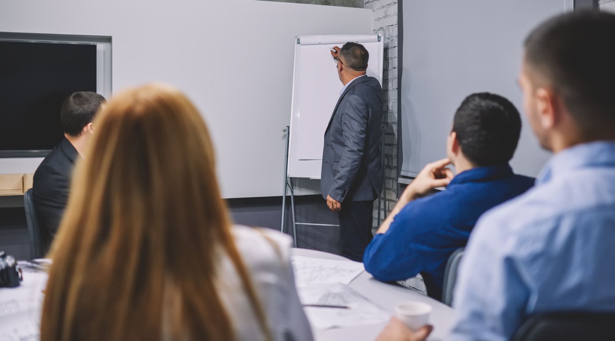 Mature corporate director in formal suit teaching colleagues explaining business strategy near fli